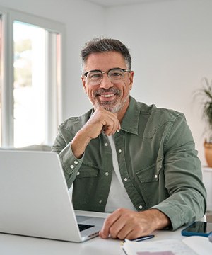 Man with glasses smiling while working on laptop