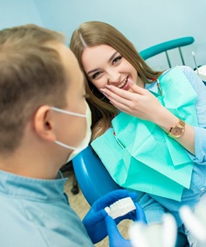 girl covering her smile in dental chair