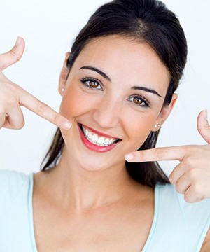 woman in white tank top pointing to her perfect smile