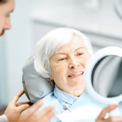 Woman with dentures in Jupiter smiling in hand mirror