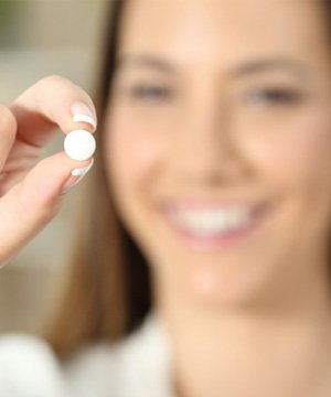 A blurred woman holding a pill between her fingers
