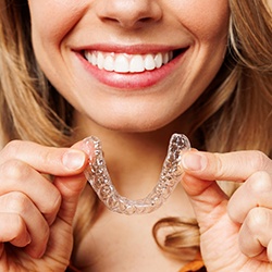 Nose-to-chest view of woman smiling and holding clear aligner