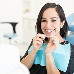 Woman in dental chair smiling holding Invisalign