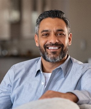 Man sitting on the couch smiling about tooth-colored fillings