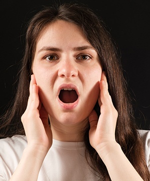 Woman touching her TMJ, suffering from symptoms of TMD