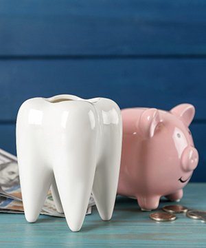  Ceramic model of tooth, a piggy bank, and money on light blue wooden table