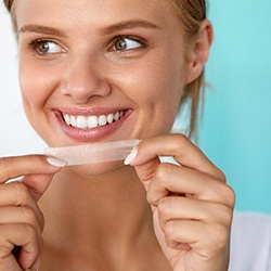 A smiling woman holding a teeth whitening strip