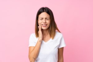 Woman experiencing tooth pain with pink background