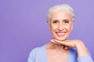 Smiling older woman with dental implants in Jupiter on purple background