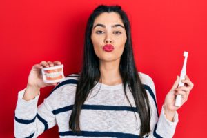 Woman holding dentures and toothbrush and pursing her lips