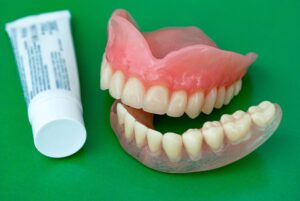 Dentures next to adhesive cream on green background